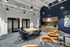 Modern shared office space with sleek wooden table, stylish blue chairs, elegant kitchenette, and chic lounge area.