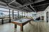 Modern apartment lounge with pool table, cozy seating area, and panoramic city views in an industrial-chic ambiance.