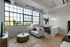 Contemporary loft-style apartment with high ceilings, large industrial windows, and modern furnishings, offering a bright and spacious living area.