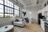 Bright and modern apartment interior with large industrial-style windows, cozy seating area, and sleek kitchen design.