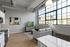 Bright and modern living space with large industrial-style windows, cozy gray sofa, and elegant decor, perfect for urban living.