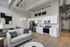 Modern open-plan apartment kitchen and living room featuring sleek white cabinetry, stainless steel appliances, and stylish contemporary decor.