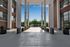 Modern apartment entrance with tall columns, large windows, and lush greenery against a bright blue sky.