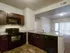 3-Bedroom Apartments in Kansas City, Missouri - Steeplechase - Standard Homes Kitchen with 9-Foot Ceiling, Wood-Style Flooring, Granite Countertops, Customized Cabinetry, Double-Sink Breakfast Bar, Black Appliances Including Built-in Microwave, Stove, Dishwasher, Light Fixture, and a View of the Empty Living Room.