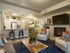 Three-Bedroom Apartments in Kansas City, Missouri - Steeplechase - Premier Homes Living Room with Wood-Style Flooring, 9-Foot Ceiling, Couch, Armchairs, Coffee Table, Fireplace, Television, Home Decor, Plant, Rugs, and a View of the Kitchen and Dining Area.