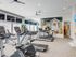 Fitness center with 3 treadmills, 2 stationary bikes, 1 elliptical, yoga balls, free weights, and 3 weight machines with large window showing connected indoor playroom