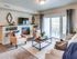 Pet-Friendly Apartments in Boise, ID - Kensington - A Model Living Room with 9-Foot Ceiling, Carpet Flooring, Built-In Entertainment Wall, Flat Screen TV, Electric Fireplace, Couch, Armchair, Coffee Table, Rug, Home Decor, Sliding Glass Door and Window with Blinds and Floor-Length Curtains, and a View of the Balcony with Outdoor Seating.