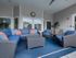1-Bedroom Apartments in Boise, ID - Kensington - Clubhouse Patio Area with Couch, Armchairs, Rectangular Coffee Table, Rug, Clock, Potted Plant, and a View of the Clubhouse Windows.
