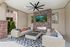 Pet-Friendly Apartments in Twin Falls, ID - Rivercrest - An Outdoor Cabana Enclosed by Two-Toned Walls Featuring 2 Long Rattan-Made Couches, 2 Adjacent Square Coffee Tables, Center Brick Wall with Flat Screen TV and Fireplace, Black Ceiling Fan, Light Fixtures, Large Rug, Plants, and 2 Open Windows Beside the Brick Wall.