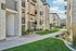 Charming apartment complex with modern stone facade, lush green walkways, and inviting balconies under a clear blue sky.