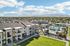 Stunning aerial view of modern apartment complex with scenic mountain backdrop, featuring lush green spaces and a sparkling pool area.
