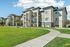 Modern apartment complex with sleek architecture, lush green lawns, and spacious balconies under a clear blue sky.