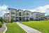 Modern apartment complex with stylish stone facade and private balconies, surrounded by lush green lawns and a clear blue sky.
