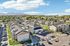 Scenic aerial view of modern apartment complex with lush green spaces, surrounded by picturesque mountains under a bright blue sky.