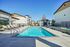 Luxurious apartment complex with a pristine outdoor swimming pool, surrounded by chic sun loungers and modern architecture under a clear blue sky.