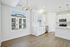 Bright and modern kitchen with sleek white cabinetry and stainless steel appliances, enhanced by large windows offering a view of the elegant neighboring building.