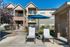 Charming apartment exterior with private balconies, lush landscaping, and inviting poolside loungers under a vibrant blue umbrella.