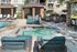 Luxurious outdoor space with inviting pool and spa, comfortable lounge chairs, and a modern barbecue area, set against stylish apartment buildings.