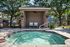 Inviting outdoor oasis with a serene hot tub next to a cozy shaded patio, surrounded by lush greenery and elegant brick architecture.