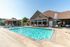 Enjoy a sunny day at this inviting apartment complex poolside with cozy loungers, shaded tables, and a charming brick clubhouse.