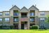 Charming multi-story apartment building with private balconies, brick and siding facade, and well-maintained green lawn, perfect for modern living.