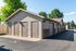 Charming outdoor view of spacious individual storage units with beige doors and red brick accents, surrounded by lush greenery and clear blue skies.