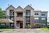 Charming three-story apartment building with modern balconies, surrounded by lush greenery and vibrant landscaping.
