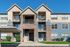 Charming three-story apartment building with modern architecture, private balconies, and elegant brick detailing under a clear blue sky.