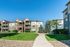 Charming apartment complex featuring three-story buildings with balconies, surrounded by lush green lawns and walking paths under a clear blue sky.