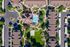 Aerial view of charming apartment complex showcasing a central pool, lush green spaces, and ample parking surrounded by modern townhouses.