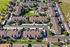 Aerial view of a charming residential complex featuring beautifully landscaped gardens, a central pool, and spacious brown-roofed buildings surrounded by greenery.