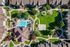 Aerial view of a modern apartment complex featuring lush green spaces, a sparkling swimming pool, a basketball court, and a children's playground.