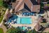 Aerial view of a modern apartment complex featuring a sparkling swimming pool surrounded by sun loungers, umbrellas, and lush greenery, offering a relaxed and luxurious outdoor experience.