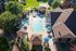 Aerial view of a beautiful community swimming pool with sun loungers, umbrellas, and lush green surroundings, perfect for relaxation and leisure.