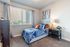 Dog-Friendly Townhomes in St. George, UT - Grayhawk Apartments at River's Edge - Cozy Bedroom With Tufted Headboard, Large Window With Blinds And Curtains, Nightstand Lamp, And Soft Carpet.
