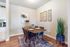 Chic dining area with elegant table setup, modern art pieces, and a lush plant accent on warm wood flooring.