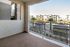 Charming apartment balcony with stone accents, overlooking a lush courtyard with palm trees and modern apartment buildings.
