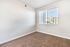 Bright empty room with plush carpeting, white walls, and large window with blinds, offering a view of neighboring buildings.