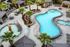Luxurious resort-style apartment complex with a stunning freeform pool, surrounded by lush palm trees and elegant outdoor seating areas.