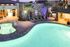 Inviting nighttime view of a luxurious swimming pool and spa area, surrounded by palm trees and cozy lounge chairs, offering a perfect relaxation spot.
