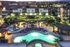 Vibrant apartment complex at night featuring a luxurious pool with colorful lighting, surrounded by lush greenery and modern buildings.