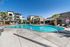 St. George, UT, Townhomes with attached Garage - Grayhawk Apartments at River's Edge - Resort Style Pool With Palm Trees, Sundeck Lounge Chairs, And Clubhouse Surrounded By Apartment Buildings.