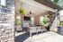 Charming outdoor lounge area with rustic stone fireplace, ceiling fan, and vibrant hanging plants, perfect for relaxation and entertaining.