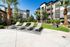 Luxurious apartment complex with sun-drenched lounge chairs, manicured gardens, and towering palm trees, offering a tranquil outdoor retreat.