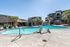 Inviting apartment complex featuring a sparkling swimming pool surrounded by palm trees, modern architecture, and ample seating for relaxation.