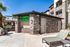 Inviting outdoor space featuring a modern apartment building with a 'Rent Me' sign, lush greenery, and comfortable lounge chairs under a bright blue sky.