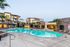 Luxurious apartment complex with a sparkling outdoor pool, modern amenities, and palm tree landscaping under a serene sky.