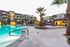 Luxurious apartment complex with palm trees and a sparkling pool, featuring modern architecture and inviting outdoor amenities in a resort-like setting.