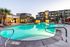 Luxurious apartment complex with an inviting, illuminated outdoor pool surrounded by palm trees and lounging areas.