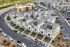 Aerial view of a modern apartment complex with a row of stylish townhouses, ample parking, and lush green surroundings.
